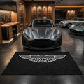Aston Martin garage floor mat, 5x7 ft (60x87"), silver-white Aston Martin winged crest on black background with dimensions shown.
