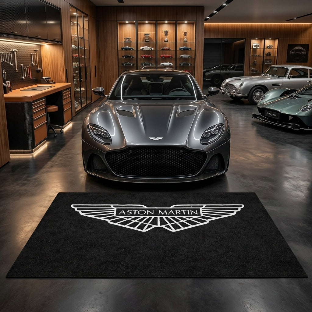 Aston Martin garage floor mat, 5x7 ft (60x87"), silver-white Aston Martin winged crest on black background with dimensions shown.
