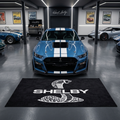 Shelby Cobra garage floor mat, 5x7 ft (60x87"), iconic coiled cobra emblem and SHELBY wordmark in white on black background with dimensions shown.